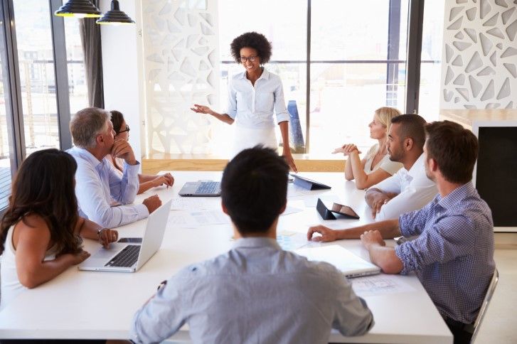 A standing woman leading a discussion at a table of her associates